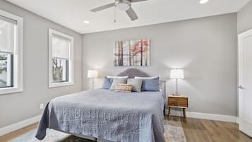 A bedroom with a bed, two bedside tables, a ceiling fan, a window, and a painting on the wall.