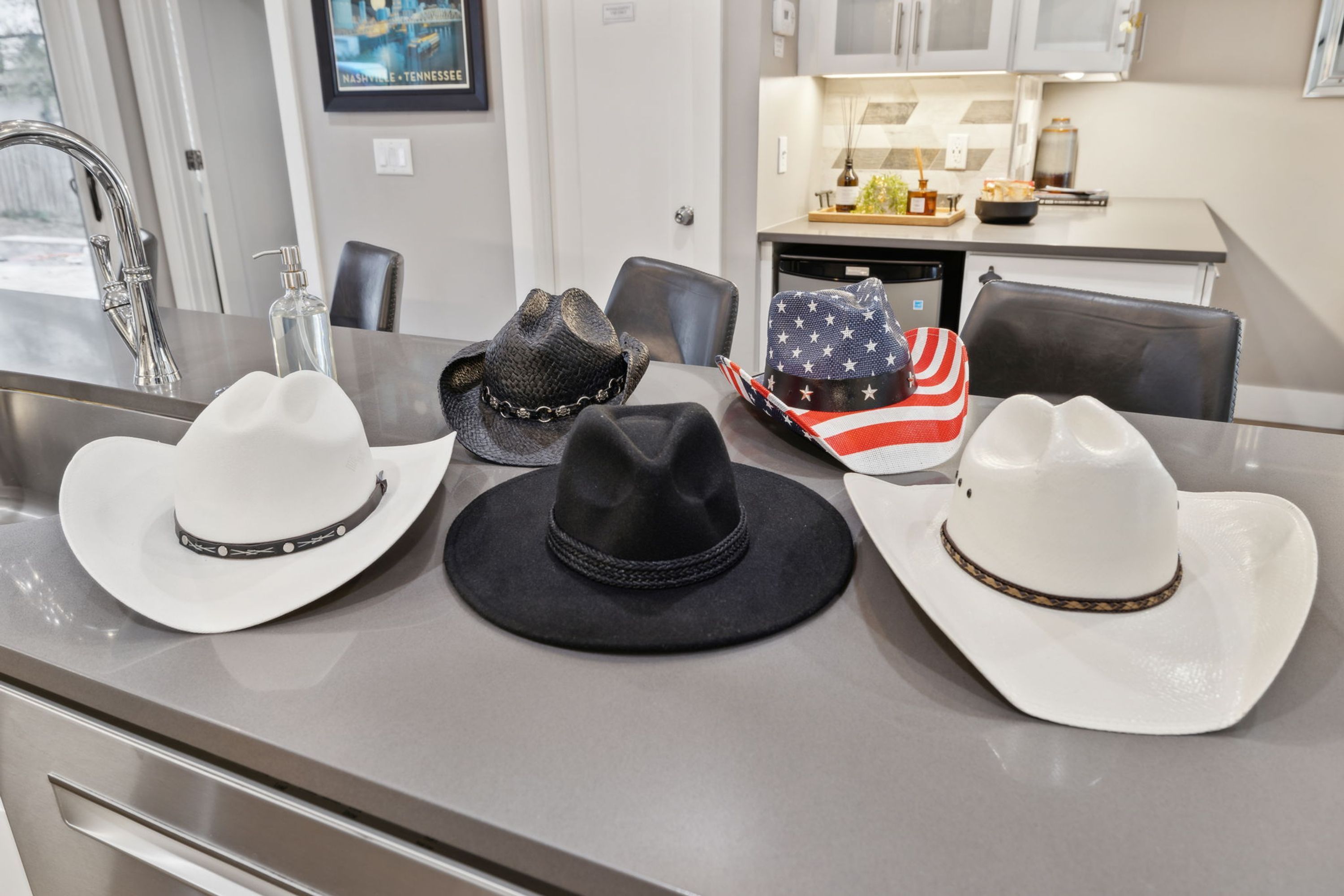 A dining area with a kitchen in the background, a sink, and three cowboy hats on the counter.