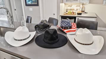 A dining area with a kitchen in the background, a sink, and three cowboy hats on the counter.