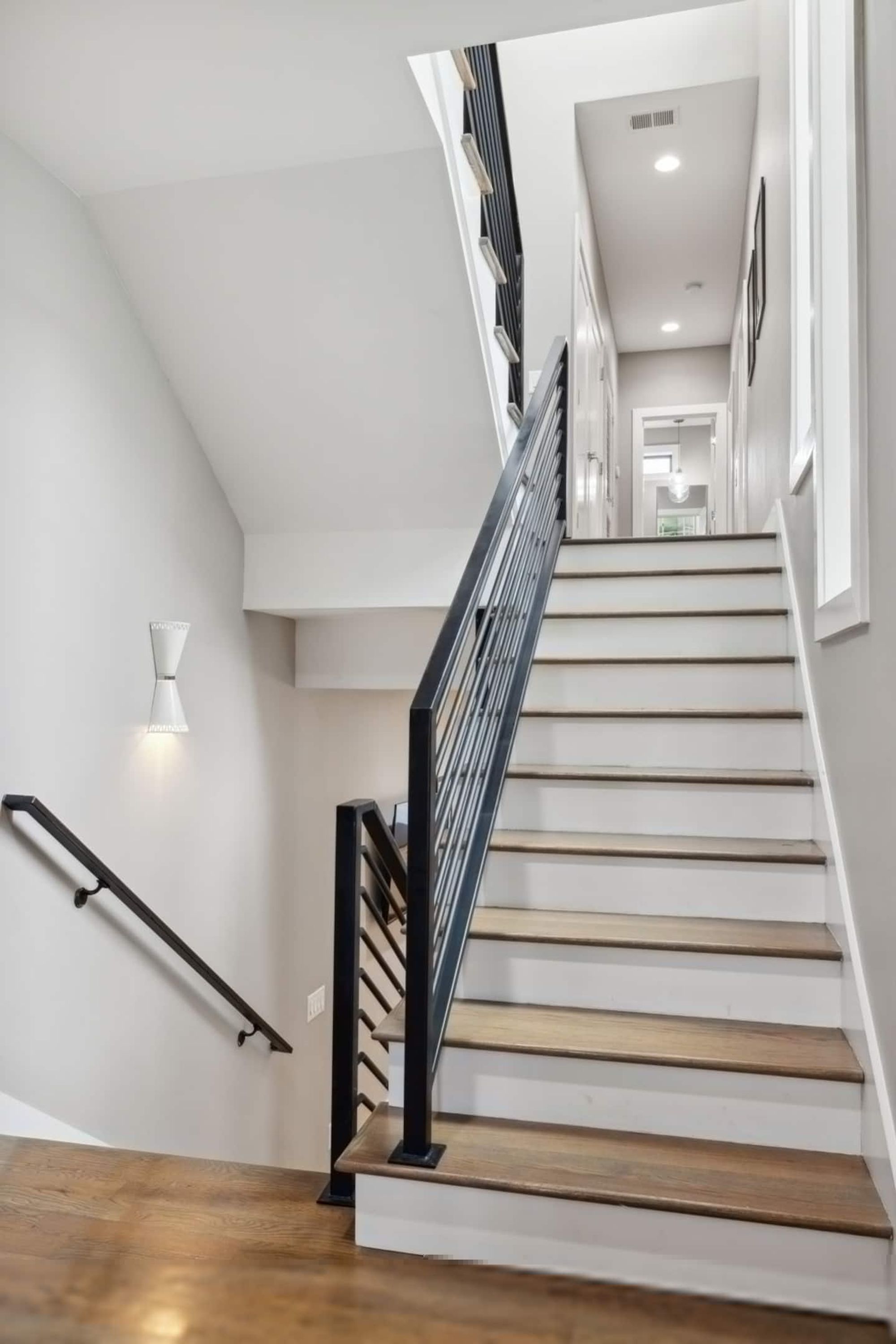 A staircase with wooden steps and a black handrail, leading to an upper floor.