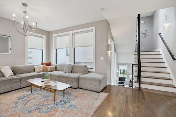 A modern living room with a sectional sofa, a coffee table, and a staircase leading to an upper level. - Hottub 2milestobway 3kbeds 5futons Safe (Nashville)