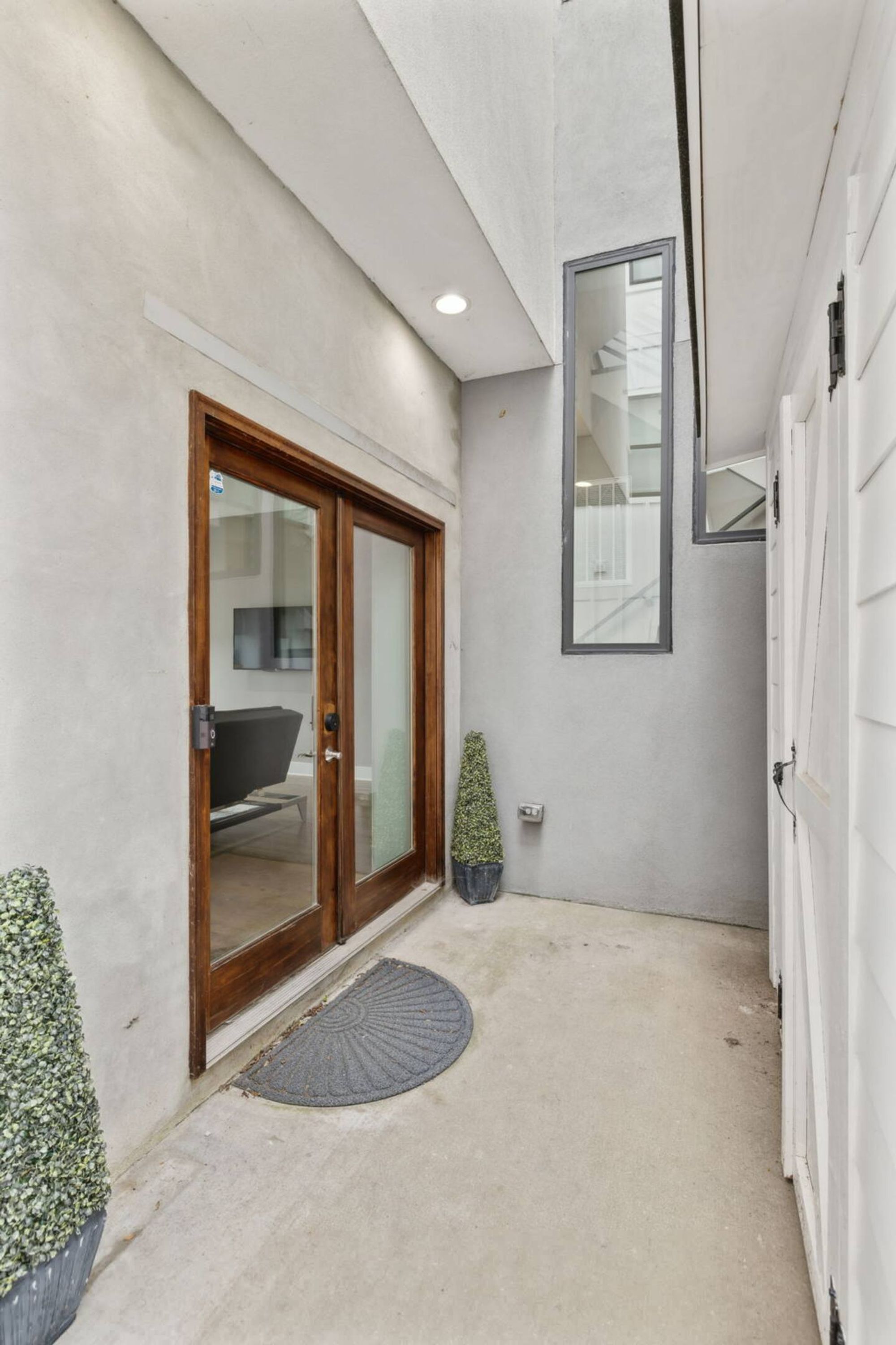 A narrow hallway with a sliding glass door leading to a room, a small potted plant, and a round doormat.