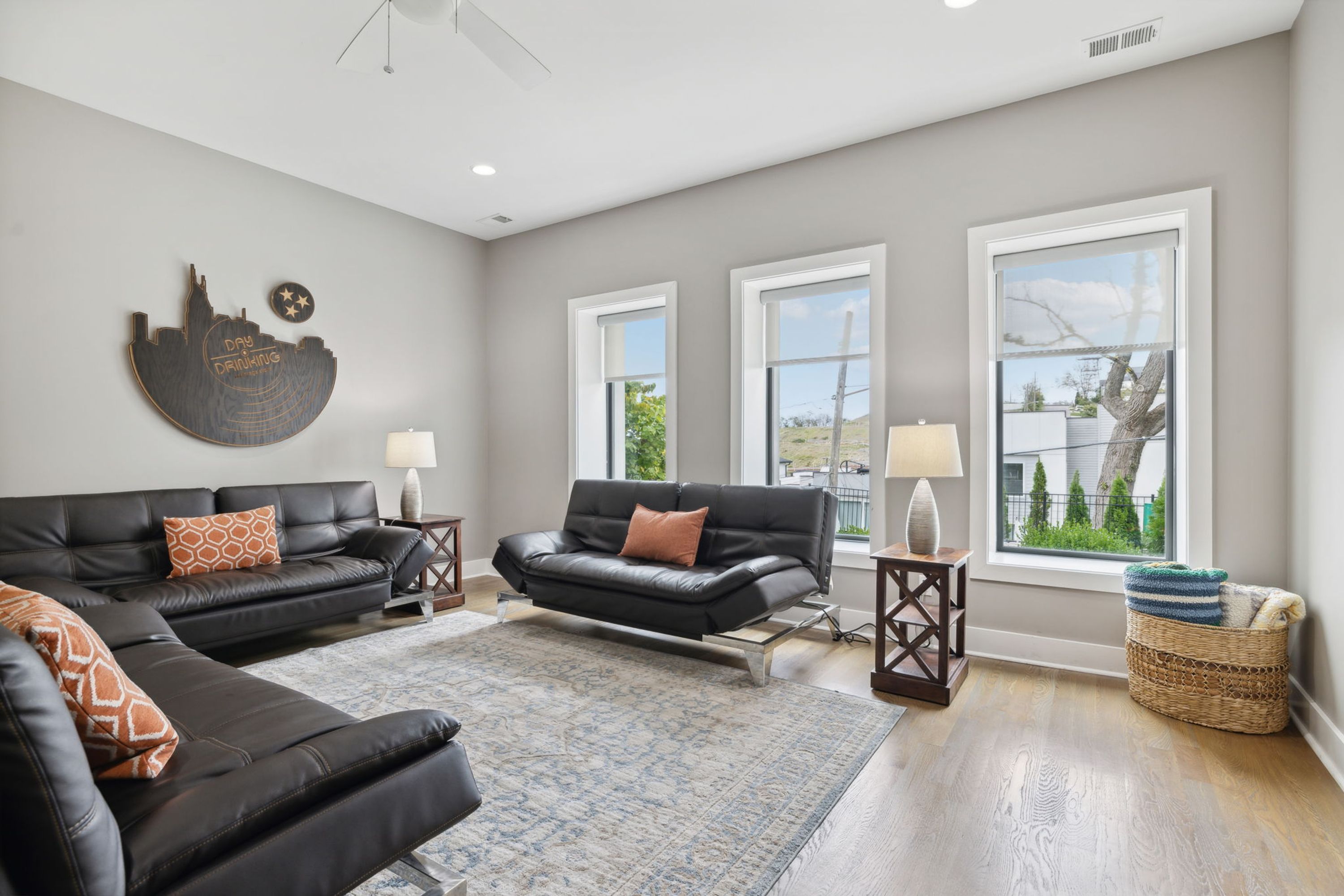 A modern living room with two black leather sofas, a patterned rug, and a cityscape wall art piece.