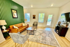 A living room with a green accent wall, a brown sofa, a patterned armchair, a coffee table, and a large rug. - Closetobroadwayairportoprymillsgameroom (Nashville)