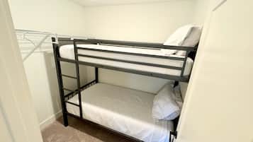 A bunk bed with a metal frame and white bedding in a small room with a carpeted floor and a white wall.