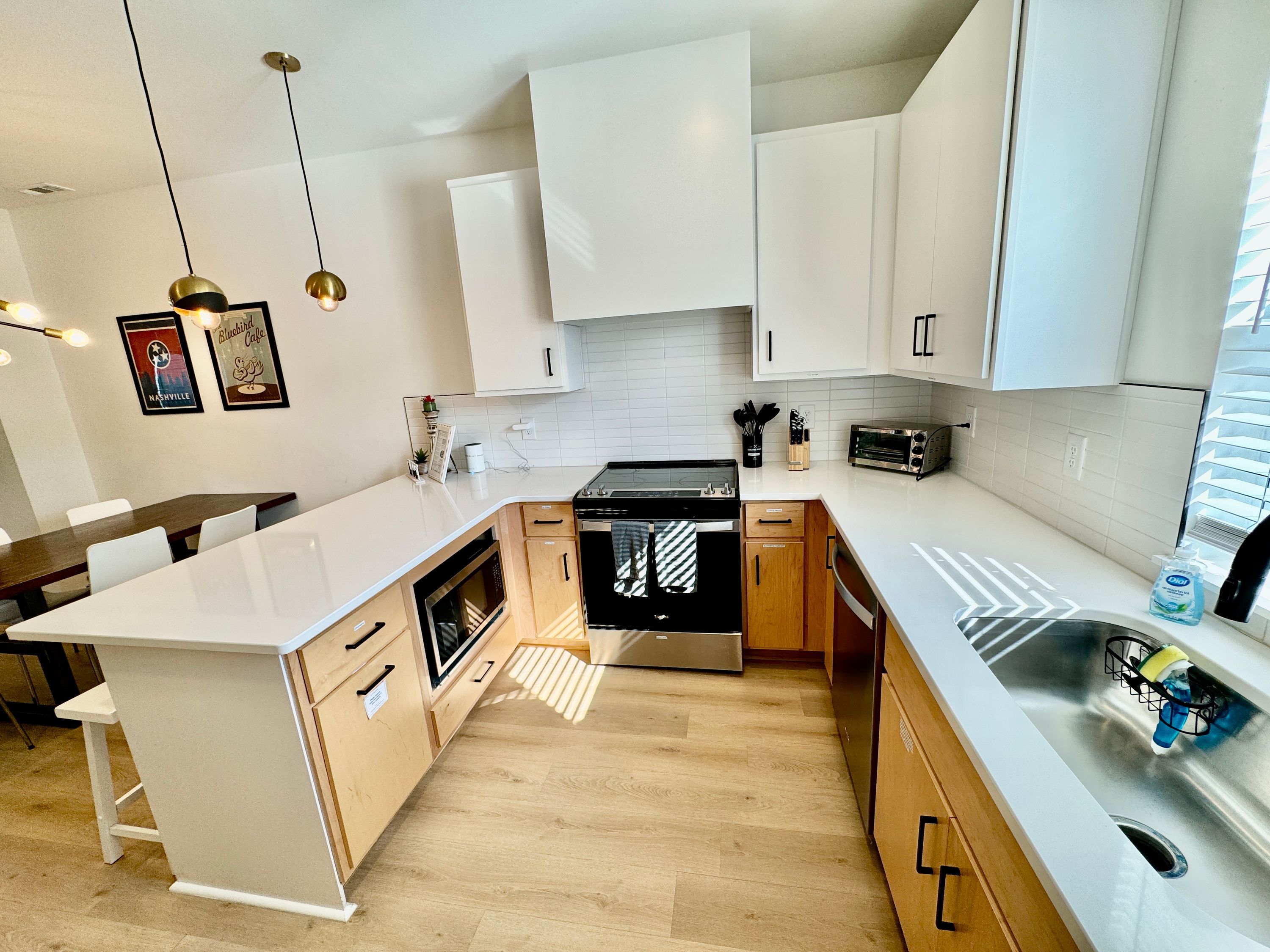 Una cocina moderna con armarios blancos, una isla central, electrodomésticos de acero inoxidable e iluminación colgante.