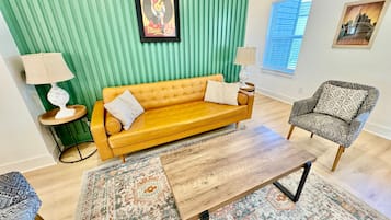 Ein Wohnzimmer mit einem gelben Sofa, einem gemusterten Sessel und einem Holztisch.
