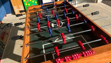 Ein Tischkicker mit roten und blauen Spielfiguren, einem Schachbrettmuster auf der Spielfläche und einem Regal mit Gegenständen im Hintergrund.