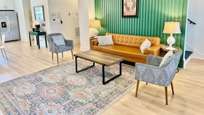 Ein modernes Wohnzimmer mit grüner Akzentwand, einem braunen Sofa, gemusterten Sesseln, einem Couchtisch und einem Teppich mit Muster.