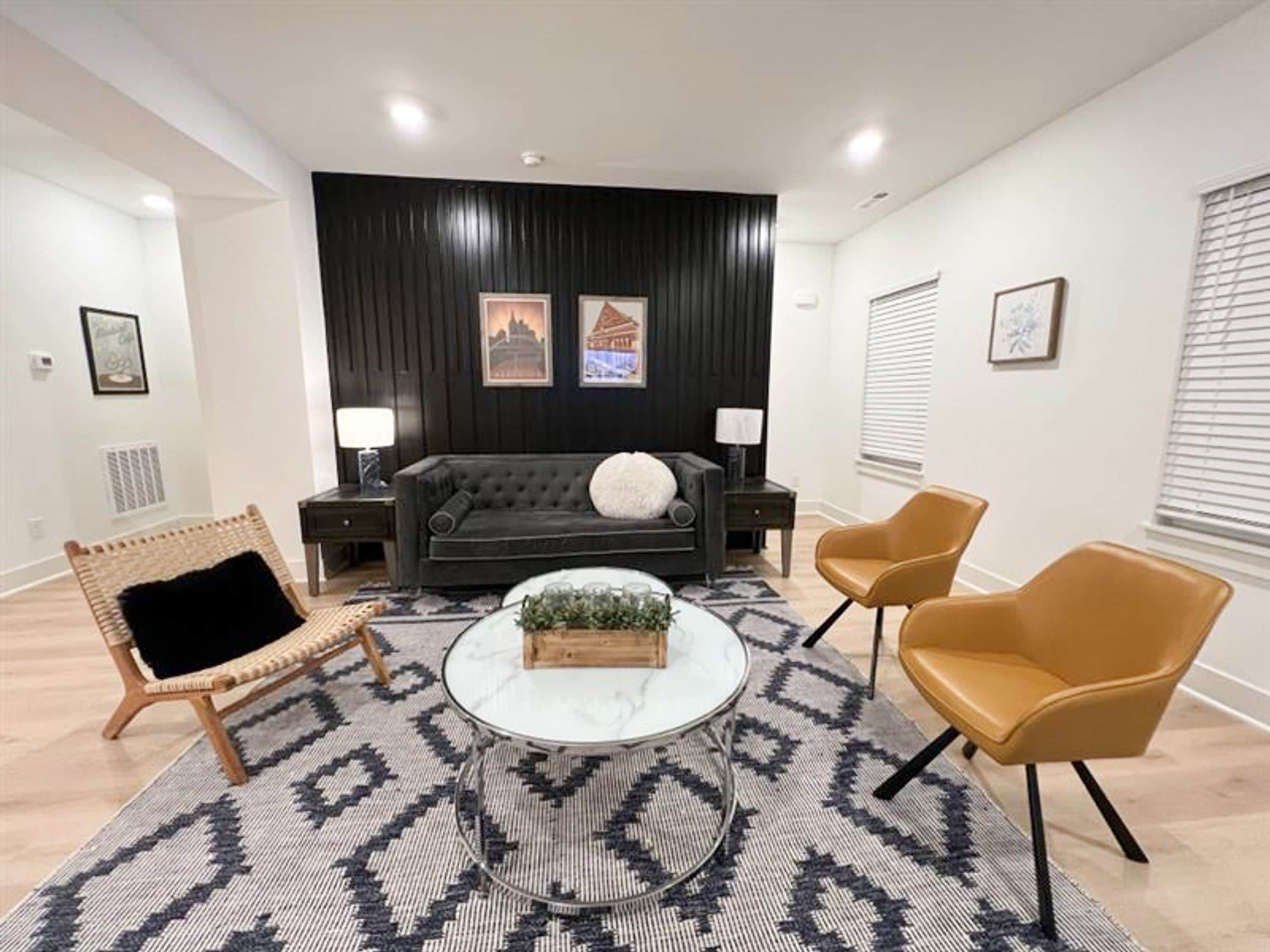 Una sala de estar moderna con un sofá, dos sillones, una mesa de centro y una alfombra estampada.