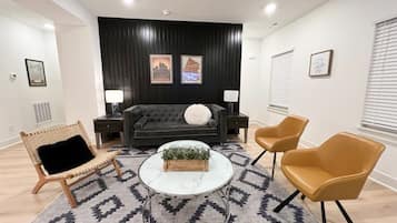 Una sala de estar moderna con un sofá, dos sillones, una mesa de centro y una alfombra estampada.