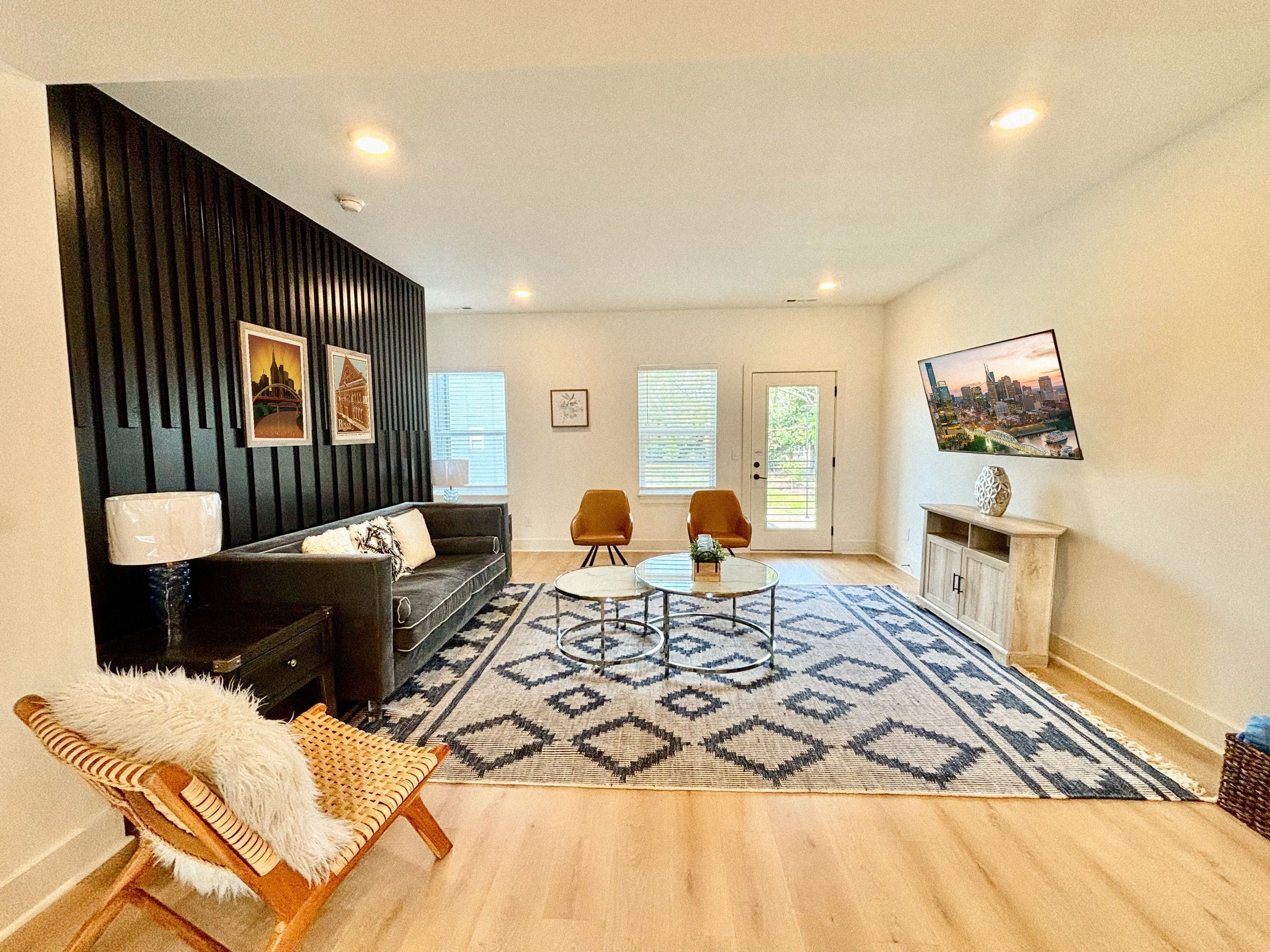 Una sala de estar moderna con una pared de acento negra, un sofá, dos sillones, una mesa de centro y una alfombra estampada.