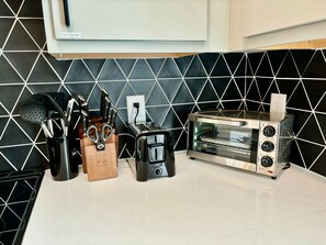 Uma cozinha com ladrilho preto e branco na parede, uma torradeira e um conjunto de facas.