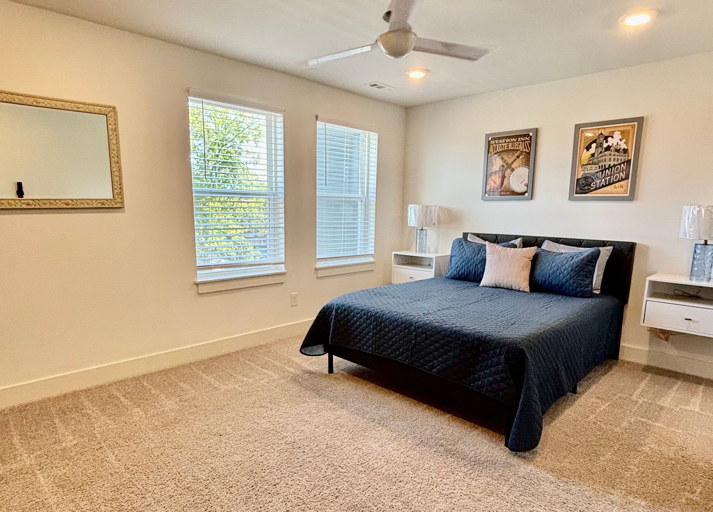 A bedroom with a bed, two nightstands, a ceiling fan, and two windows with blinds.