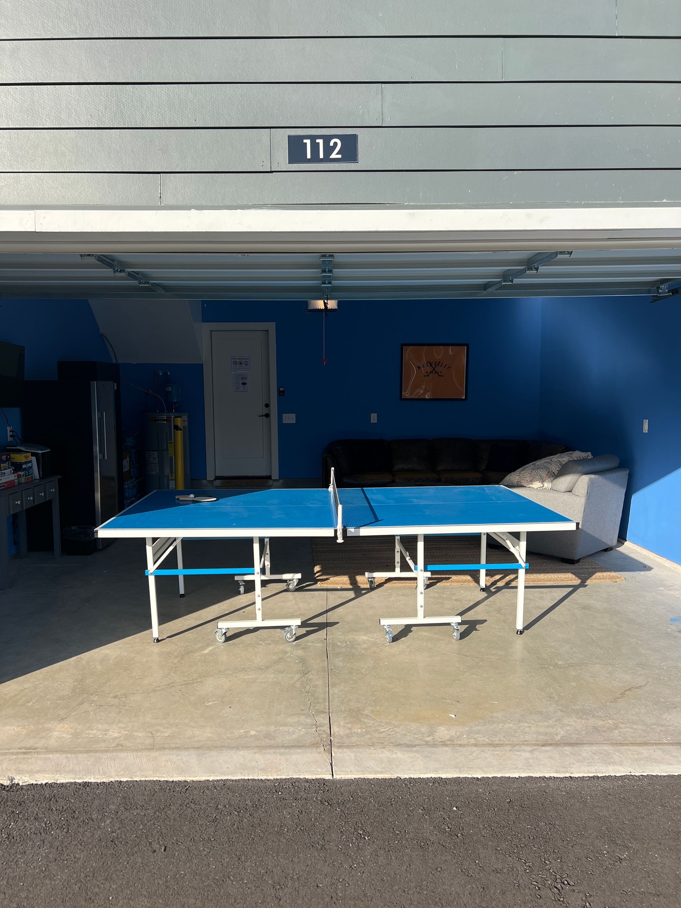 A ping pong table in a garage with a blue wall and a door marked 112.