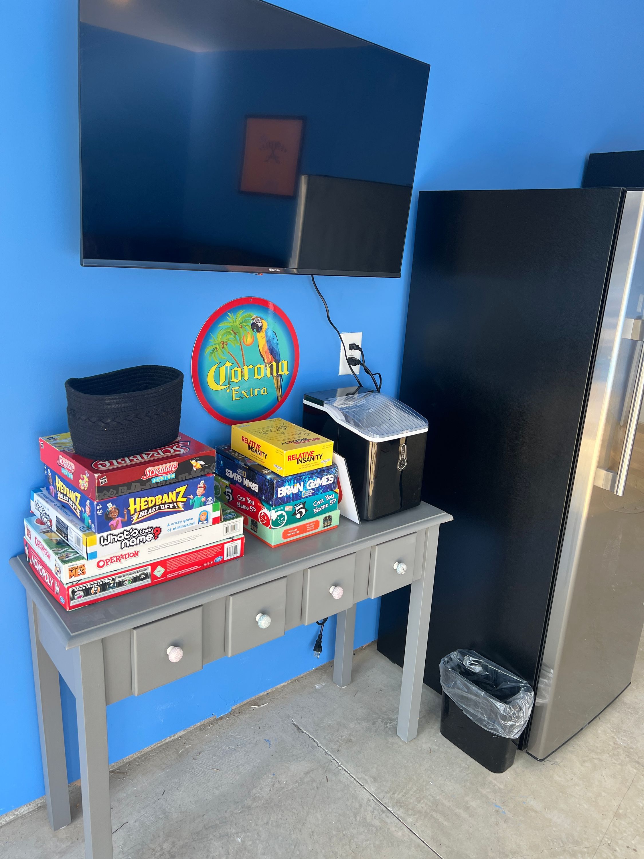 Quarto com parede azul, televisão de tela plana fixada acima de um console cinza e geladeira preta.