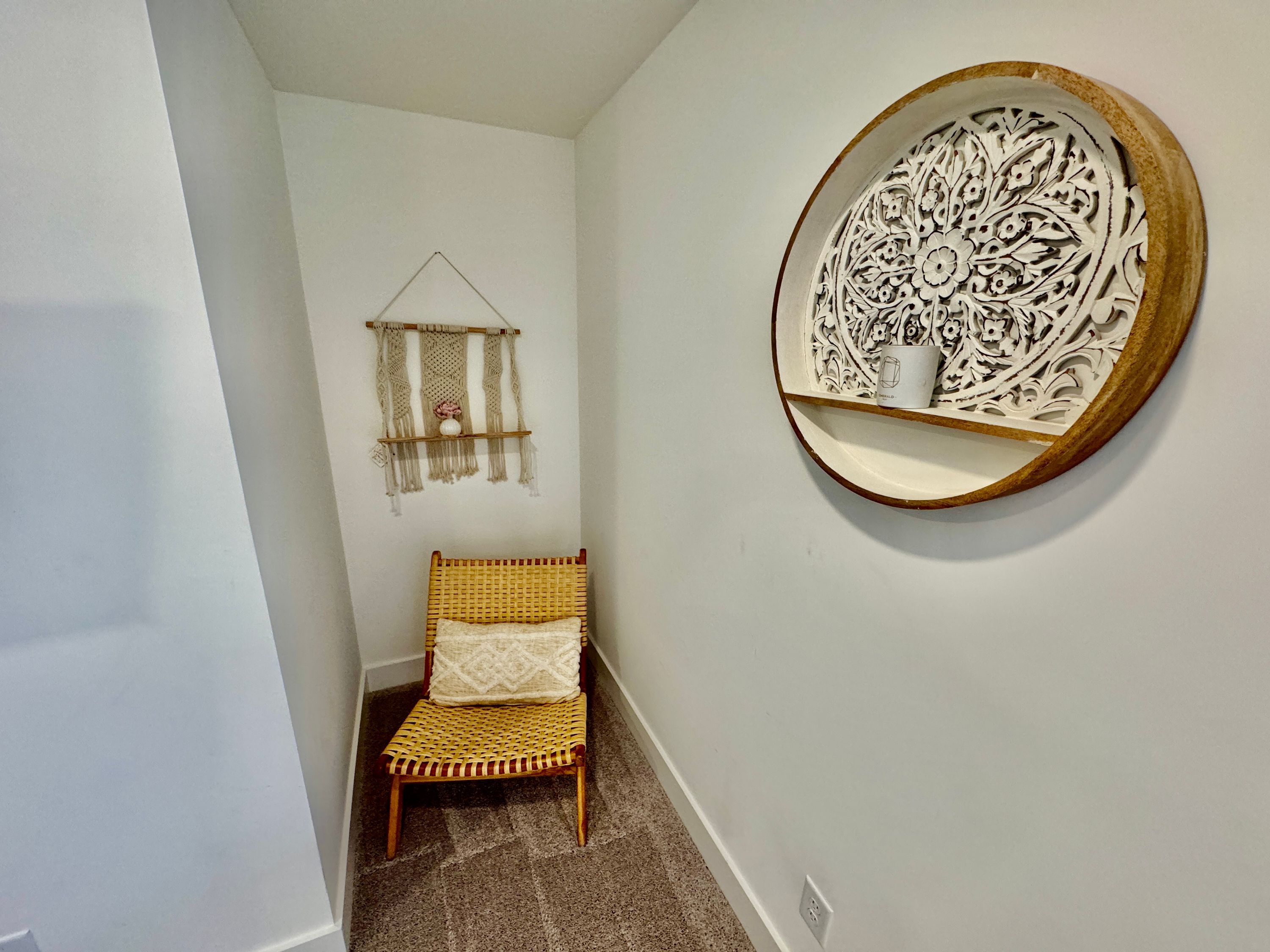 A narrow hallway with a wicker chair, a macramé wall hanging, and a decorative wooden plate on the wall.