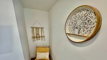 A narrow hallway with a wicker chair, a macramé wall hanging, and a decorative wooden plate on the wall.