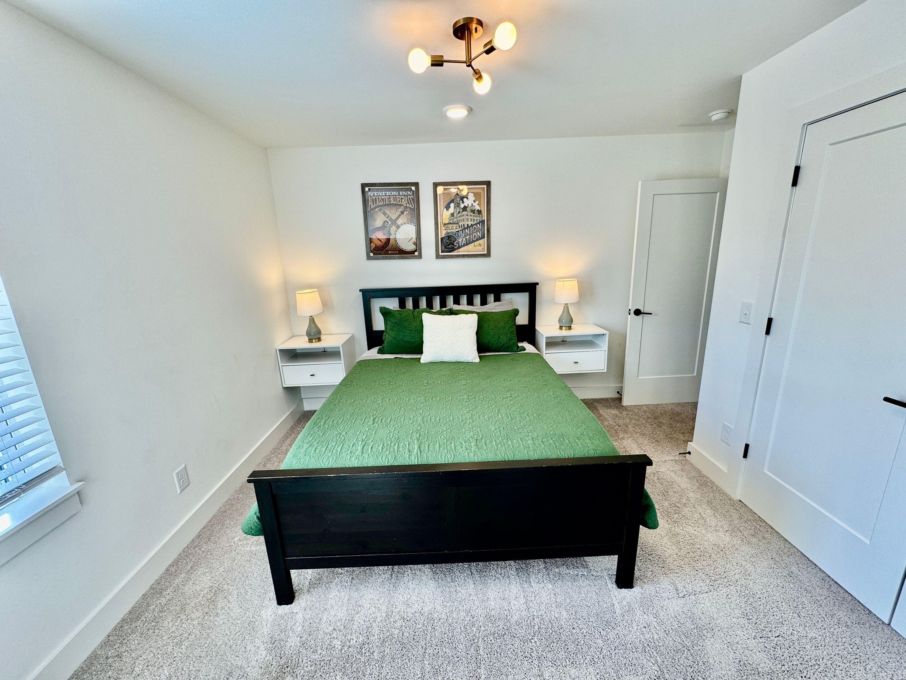 A bedroom with a bed, two nightstands, a door, and two framed pictures on the wall.