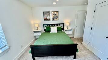 A bedroom with a bed, two nightstands, a door, and two framed pictures on the wall.