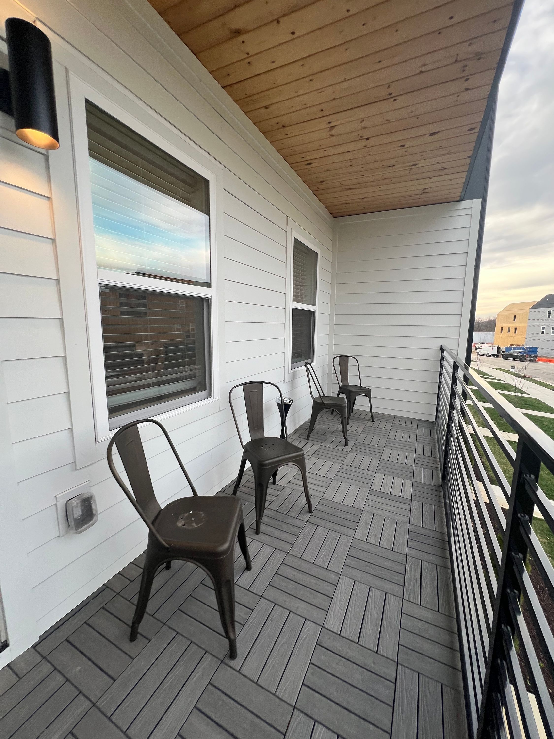 A covered porch with three metal chairs and a wooden ceiling.