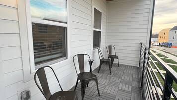 A covered porch with three metal chairs and a wooden ceiling.