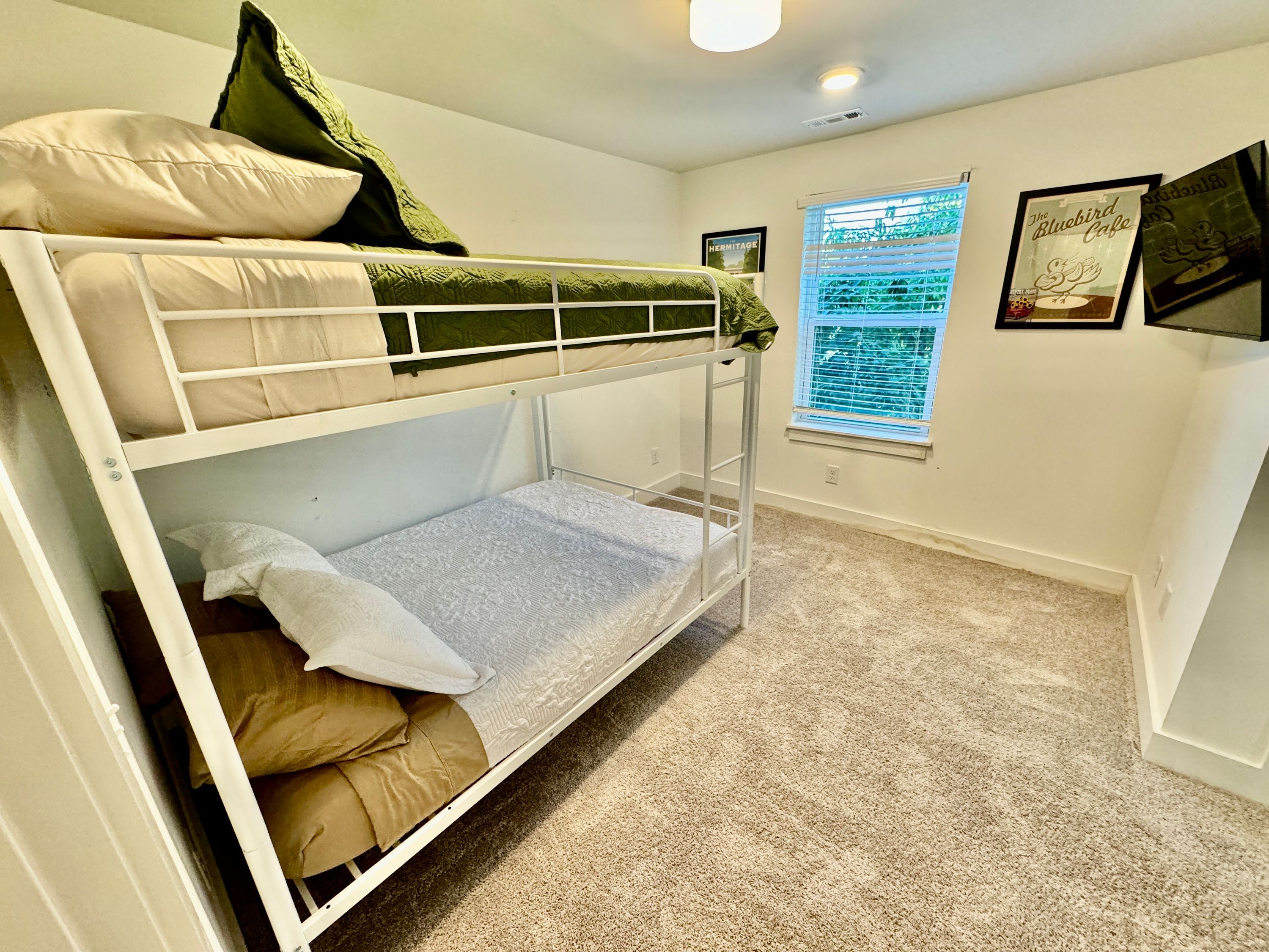 A bunk bed room with a window, a framed picture on the wall, and a carpeted floor.