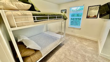 A bunk bed room with a window, a framed picture on the wall, and a carpeted floor.