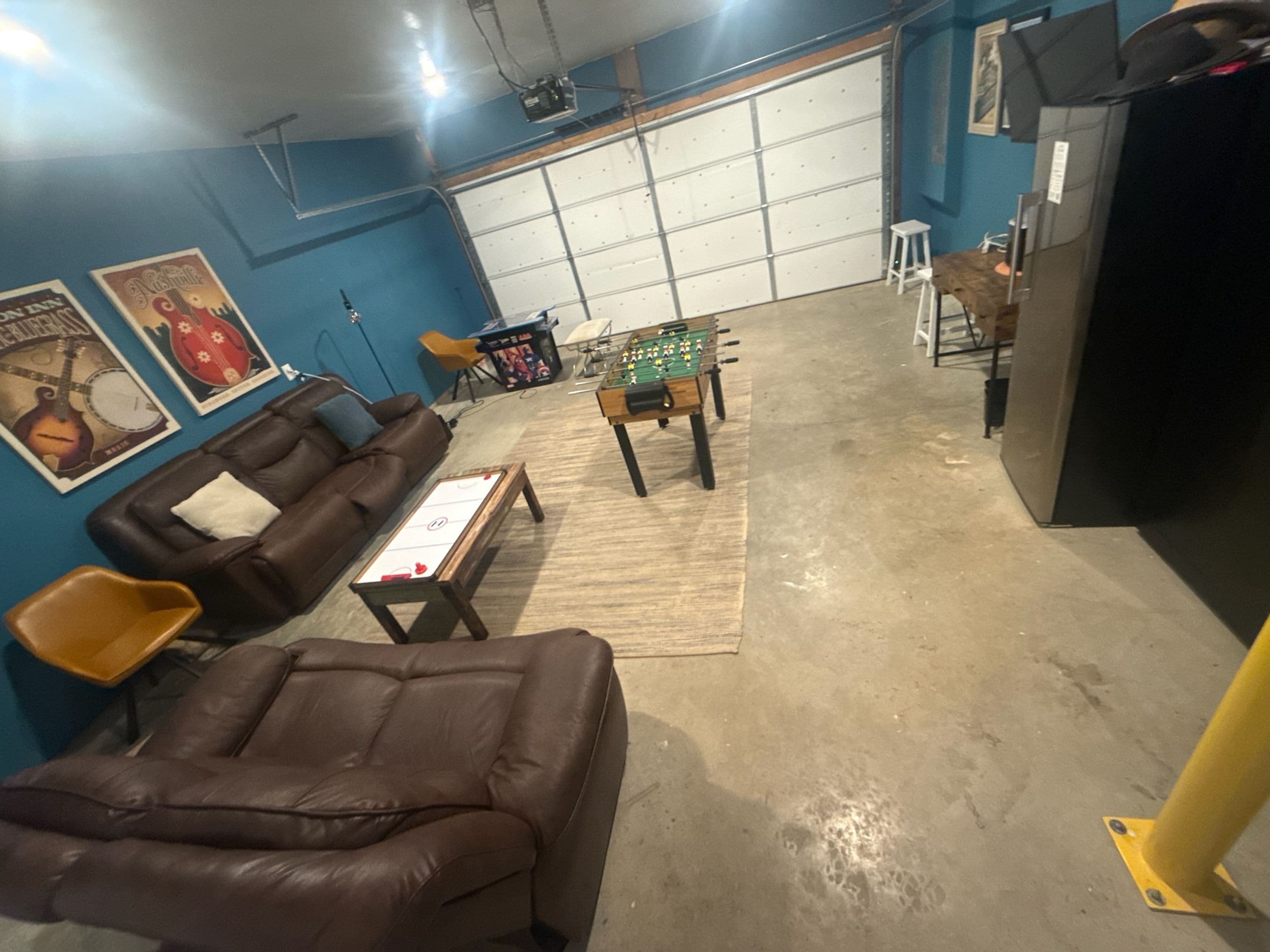 A room with a brown leather sofa, a foosball table, and a blue wall with posters.