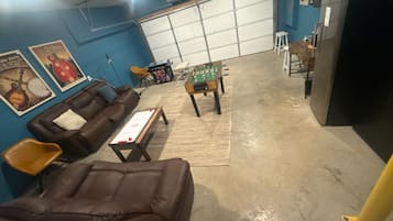 A room with a brown leather sofa, a foosball table, and a blue wall with posters.