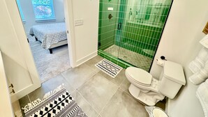 Ein Badezimmer mit Dusche und WC, sowie ein Bett im angrenzenden Raum.