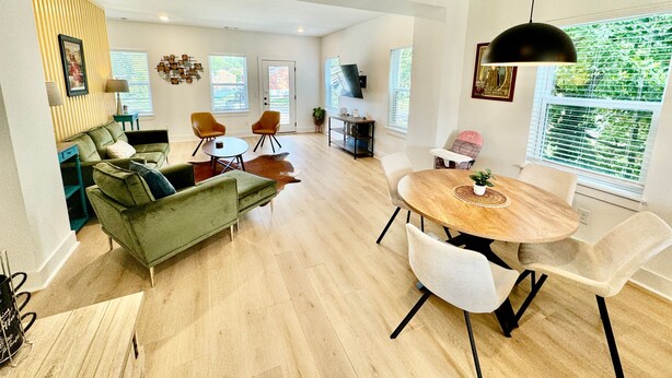 Ein geräumiges Wohnzimmer mit einem grünen Sofa, einem runden Holzesstisch und einem großen Fenster mit Jalousien.