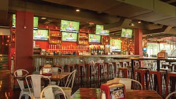 Zona de bar con varias televisiones mostrando contenido deportivo, una variedad de botellas en estantes y varias mesas y sillas para sentarse.