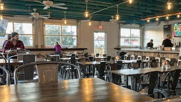 A restaurant interior with multiple tables and chairs, ceiling fans, and large windows.