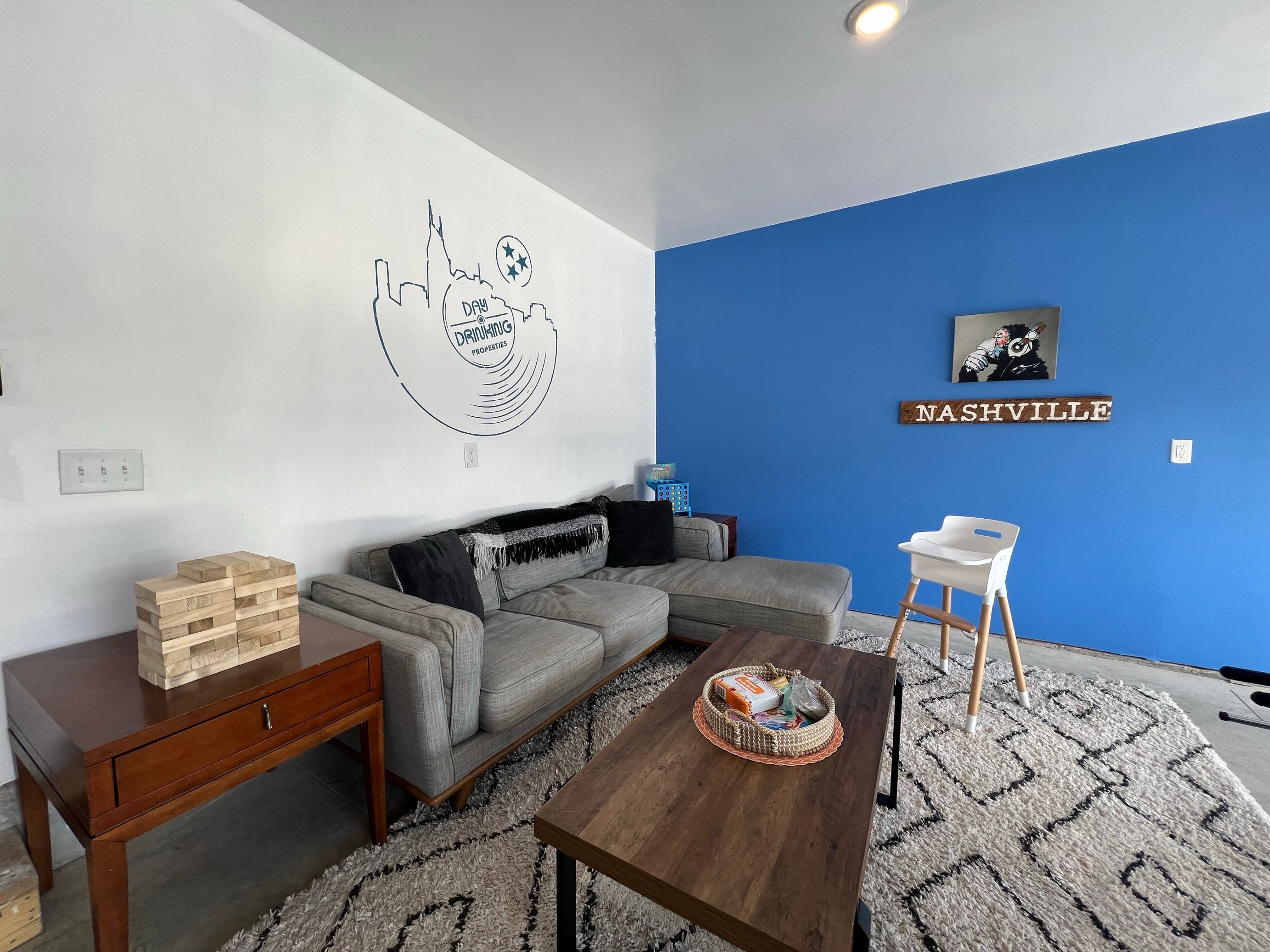 Una sala de estar con una pared azul de acento, una mesa de centro de madera, un sofá gris y una pequeña silla blanca.