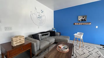 Una sala de estar con una pared azul de acento, una mesa de centro de madera, un sofá gris y una pequeña silla blanca.