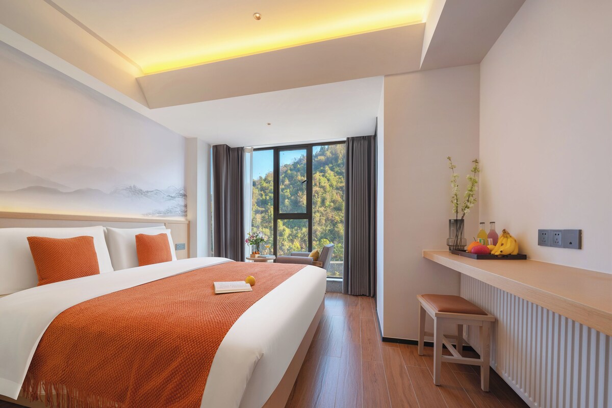 Habitación de hotel moderna con una cama grande, vistas al exterior y una pequeña zona de estar.