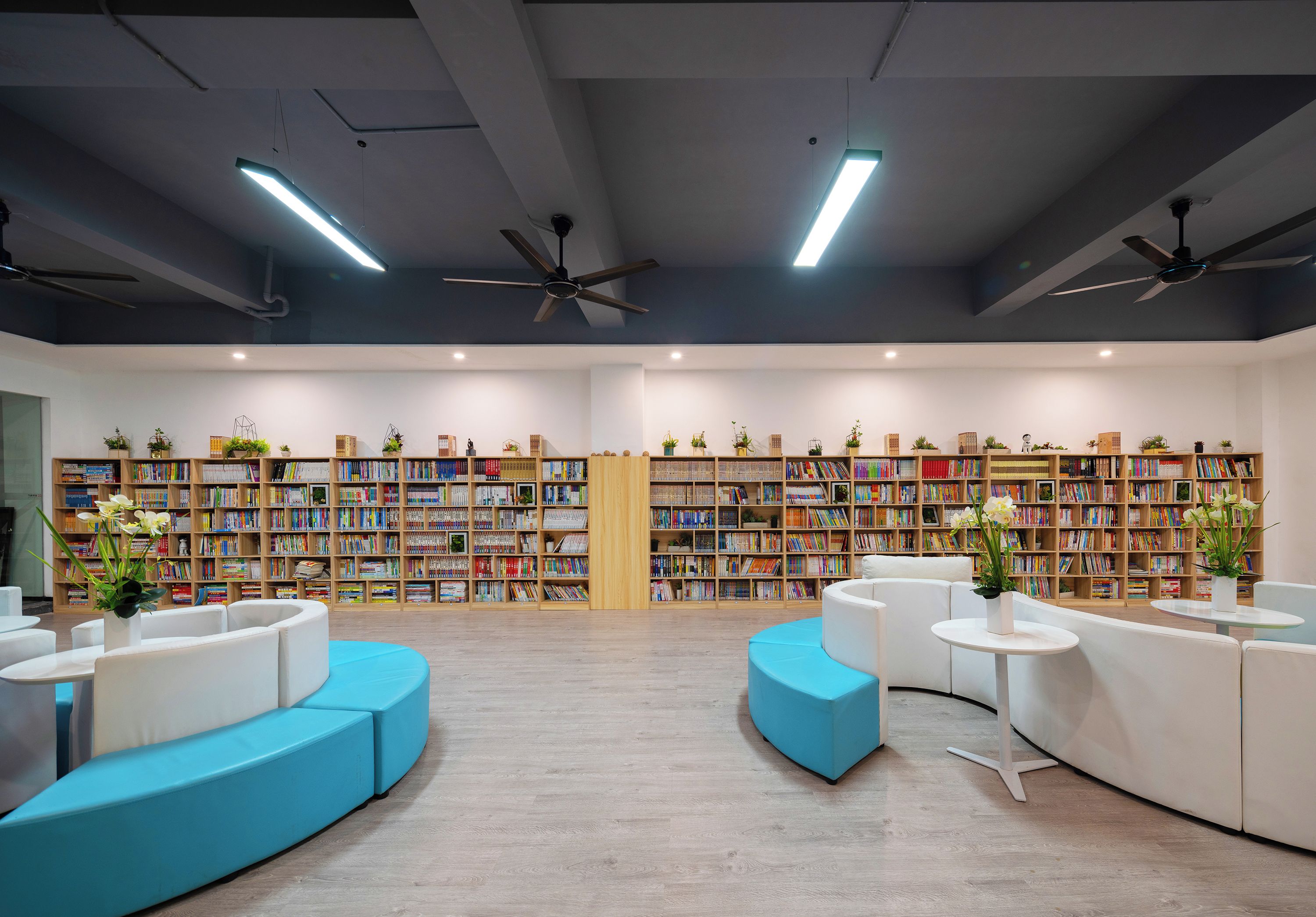 Une bibliothèque moderne dotée d’étagères, d’espaces de lecture et de ventilateurs de plafond.