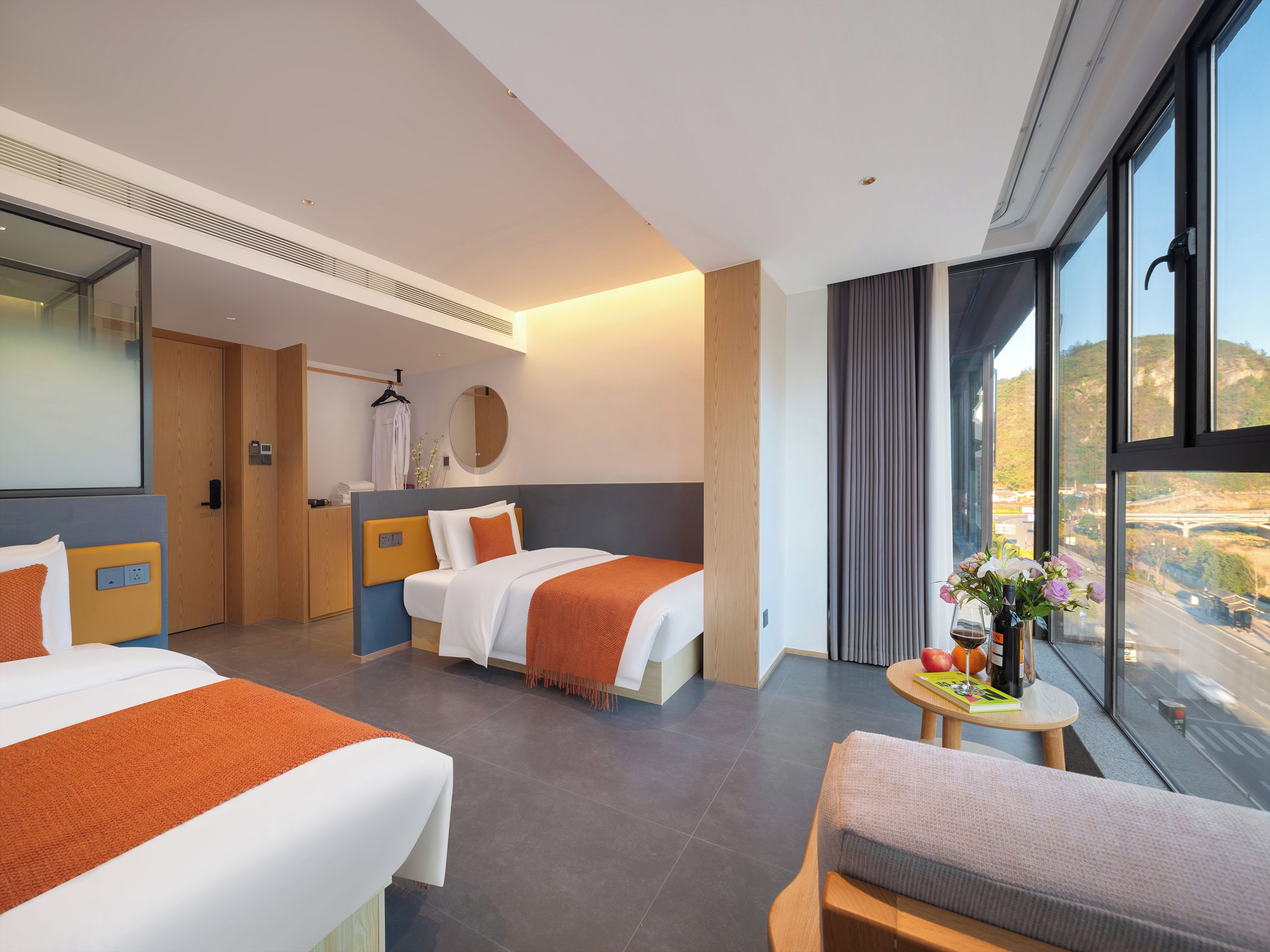 A hotel room with two beds, a sitting area, a round table with a vase of flowers, and a large window offering a view.