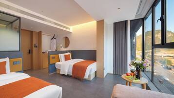 A hotel room with two beds, a sitting area, a round table with a vase of flowers, and a large window offering a view.
