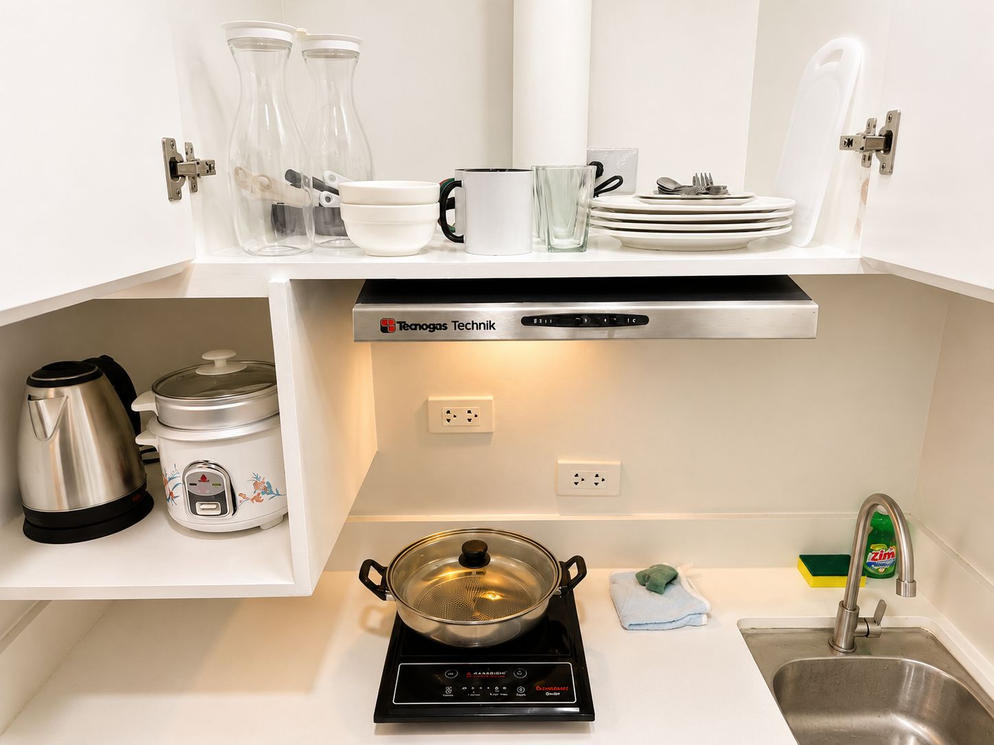 A kitchen with a stove, kettle, and various utensils.
