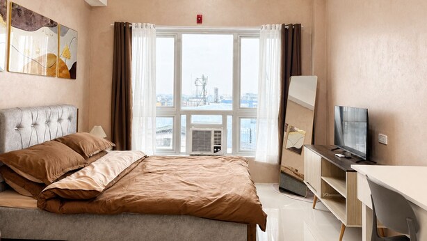 Une chambre d’hôtel avec un lit, un bureau, une télévision et une grande fenêtre avec des rideaux.