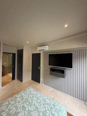 Quarto com cama, TV na parede e ar condicionado.