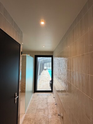 Un pasillo con paredes de baldosas, una puerta y vista a la zona de la piscina.