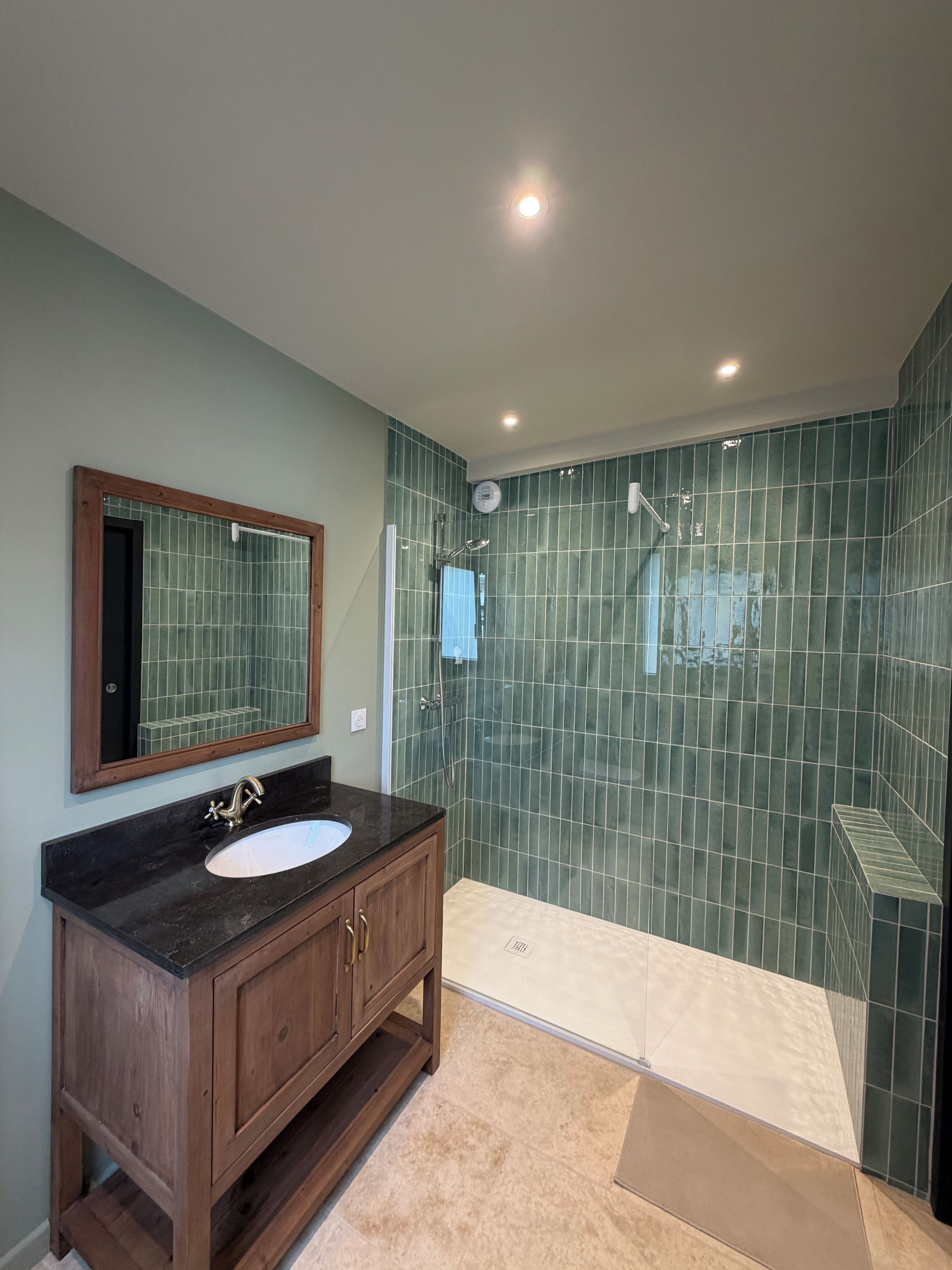 Une salle de bain avec un meuble-lavabo en bois, un évier, un miroir et un espace douche aux carreaux verts.