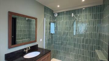 Une salle de bain avec un meuble-lavabo en bois, un évier, un miroir et un espace douche aux carreaux verts.