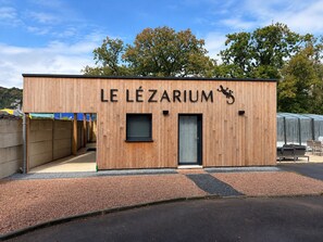 A wooden building with the name 'LE LÉZARIUM' and a lizard logo, featuring a door and a window. - The Lézarium Private Suite & Spa | Heated pool at 30°C (Saint-Aubin-lès-Elbeuf)