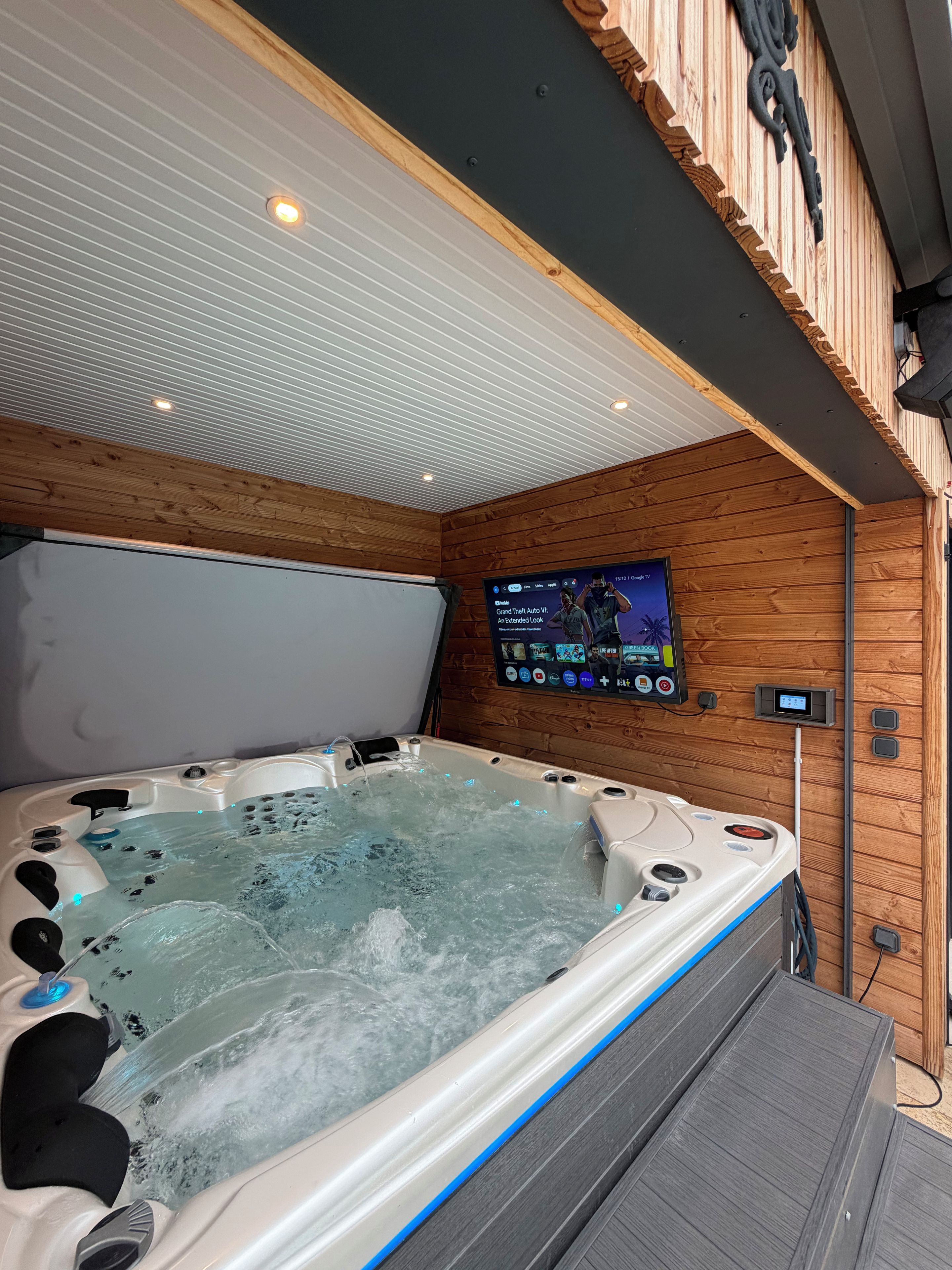 A hot tub with a wooden wall and a mounted screen displaying a show.