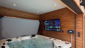 A hot tub with a wooden wall and a mounted screen displaying a show.