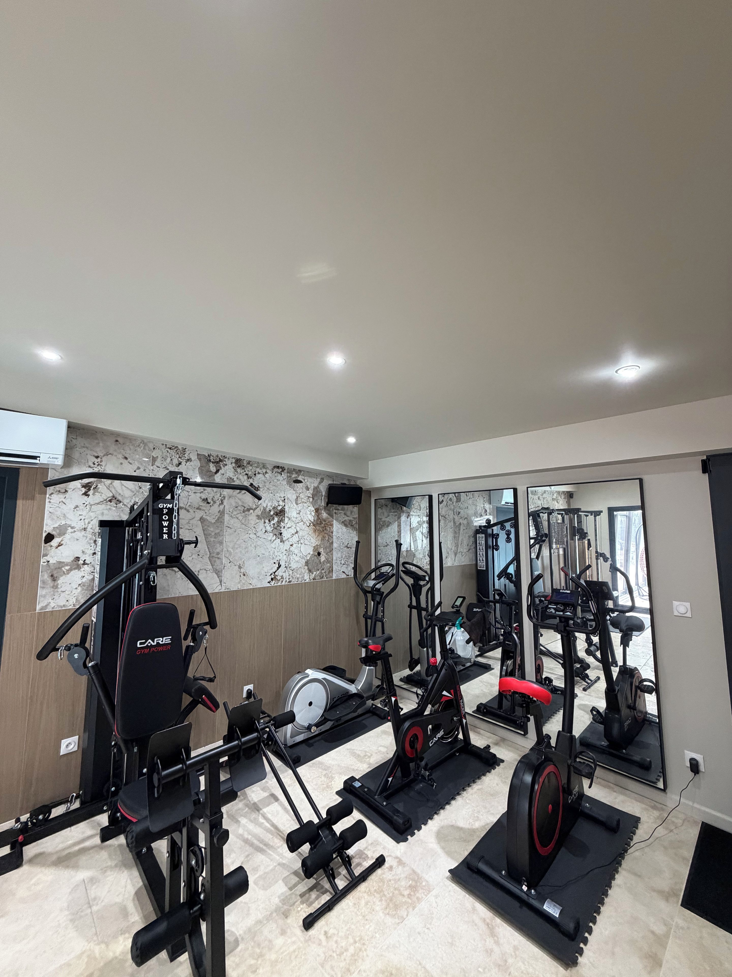 Een sportschool met diverse fitnessapparaten, waaronder een loopband, een crosstrainer en krachttoestellen.